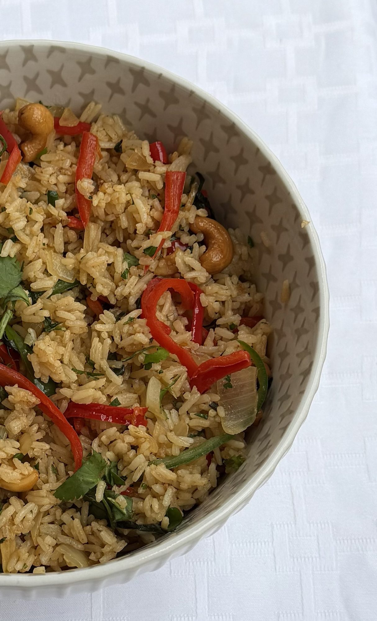 Instant Pot Thai Basil Fried Rice in a bowl topped with red bell peppers, cashews, cilantro, and fresh basil on a white tablecloth
